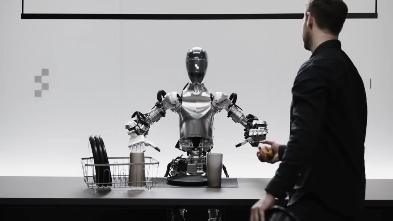 A robot sits at a table with a human standing in front of it