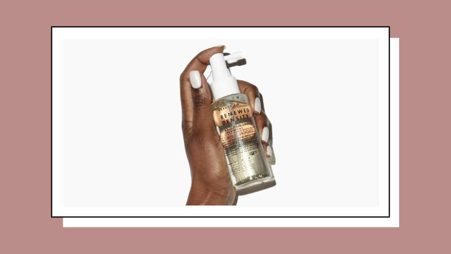 A Black woman's well-manicured hand holds a bottle of Beauty Pie's Renewed Density Anti-Hair Loss Treatment