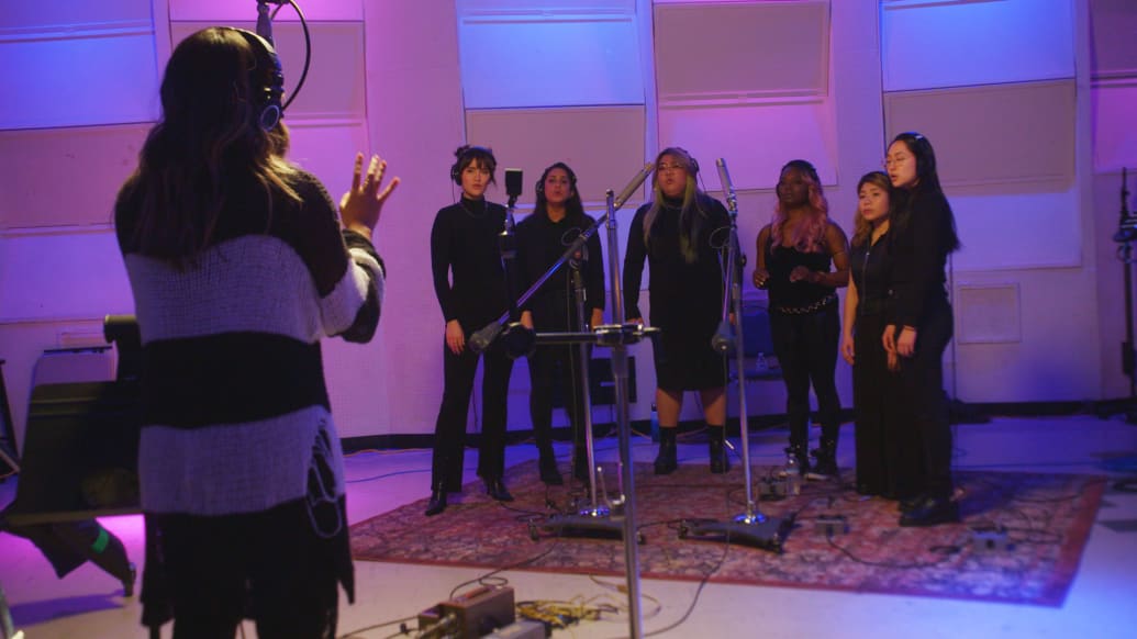 A photograph of a group of people singing in a studio.