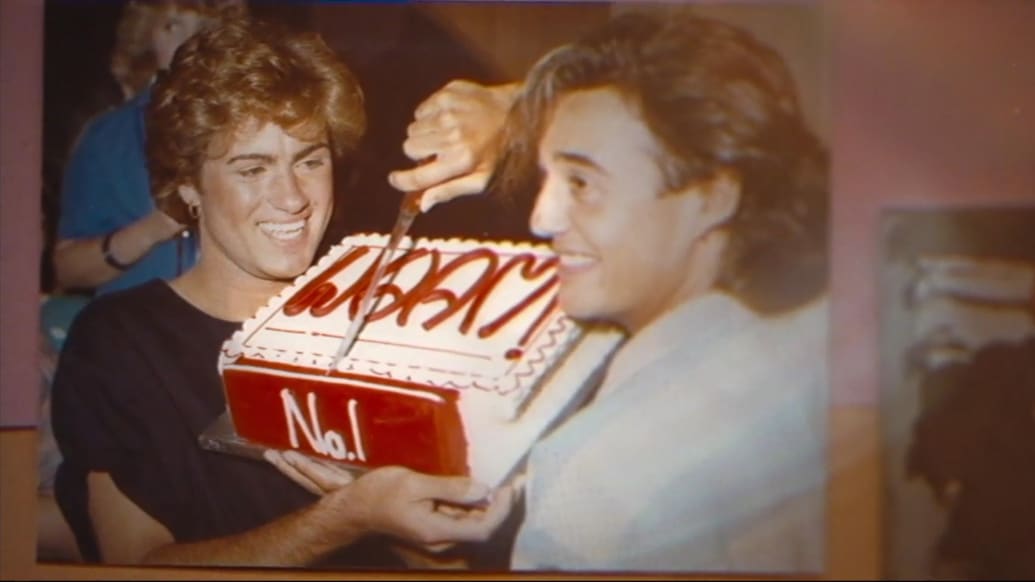 An archival photo of George Michael and Andrew Ridgeley in Wham! cutting a cake