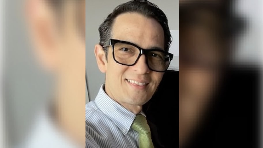 Pedro Argote smiles while wearing glasses and a shirt and tie.