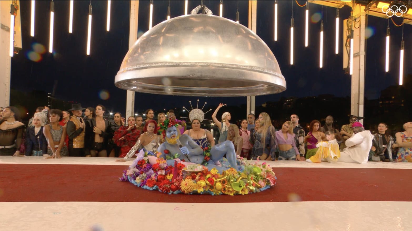 A group of drag queens behind a table with a Dionysus impersonator on the table.