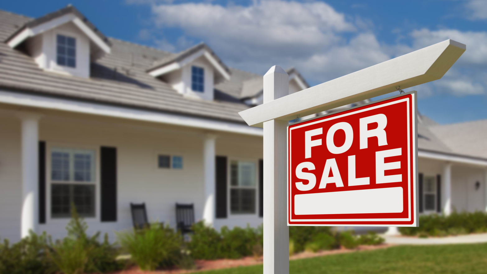 A for sale sign sits in the front yard of a white, two-story home.