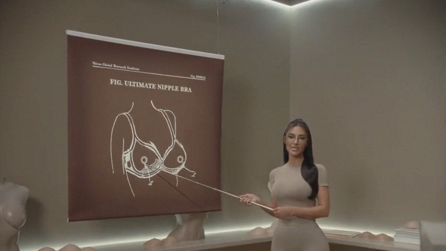 Kim Kardashian uses a pointer to direct attention to a diagram of her shapewear line's new Ultimate Nipple Bra.