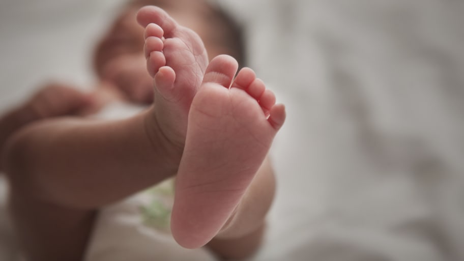 A newborn baby lying down with her feet in the air.