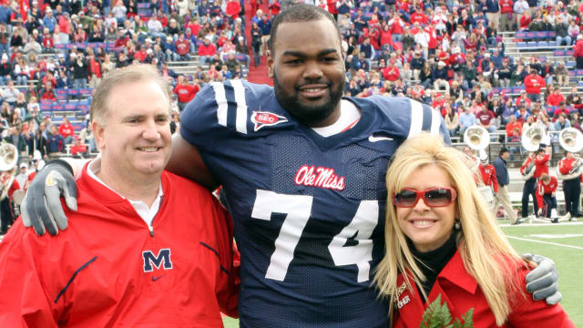 Michael Oher in uniform at the University of Mississippi smiles between Sean and Leigh Anne Tuohy.