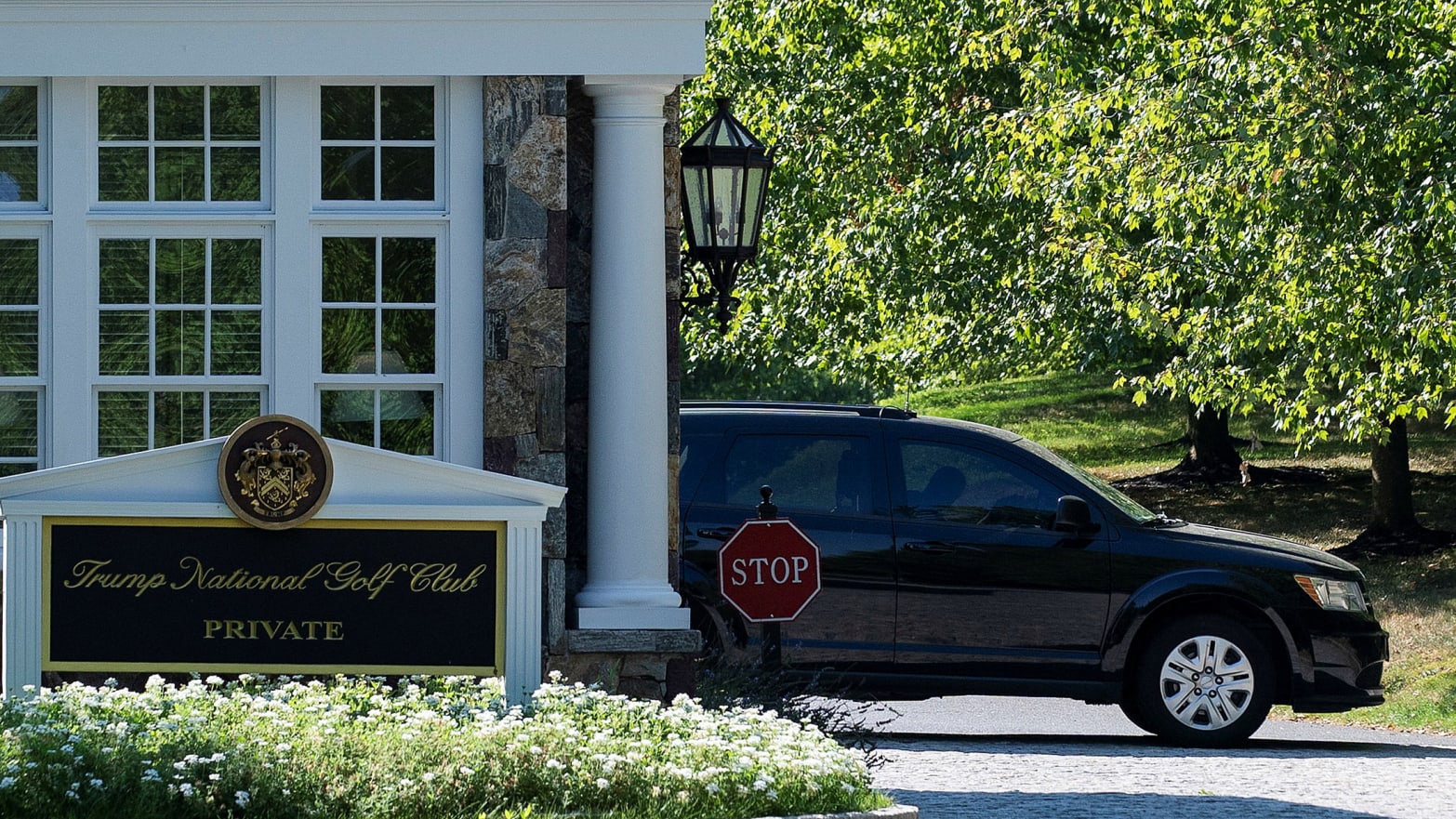 A black car pulls out from behind a sign that says Trump National Golf Club.