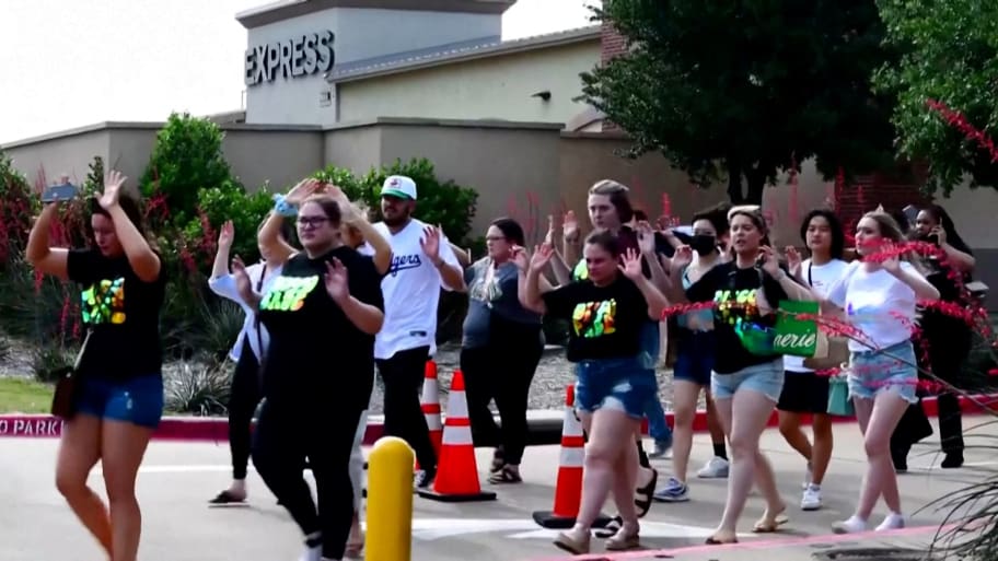 Shoppers leave with their hands up after police responded to a gunman who shot and killed eight people and wounded at least seven others at Allen Premium Outlets mall north of Dallas.