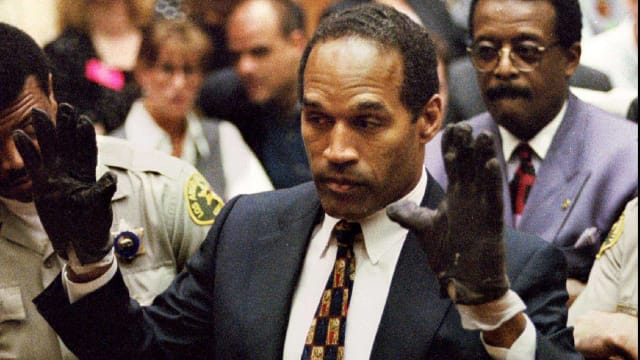 O.J. Simpson famously raises his hands as he puts on gloves in front of the jury during his double-murder trial.