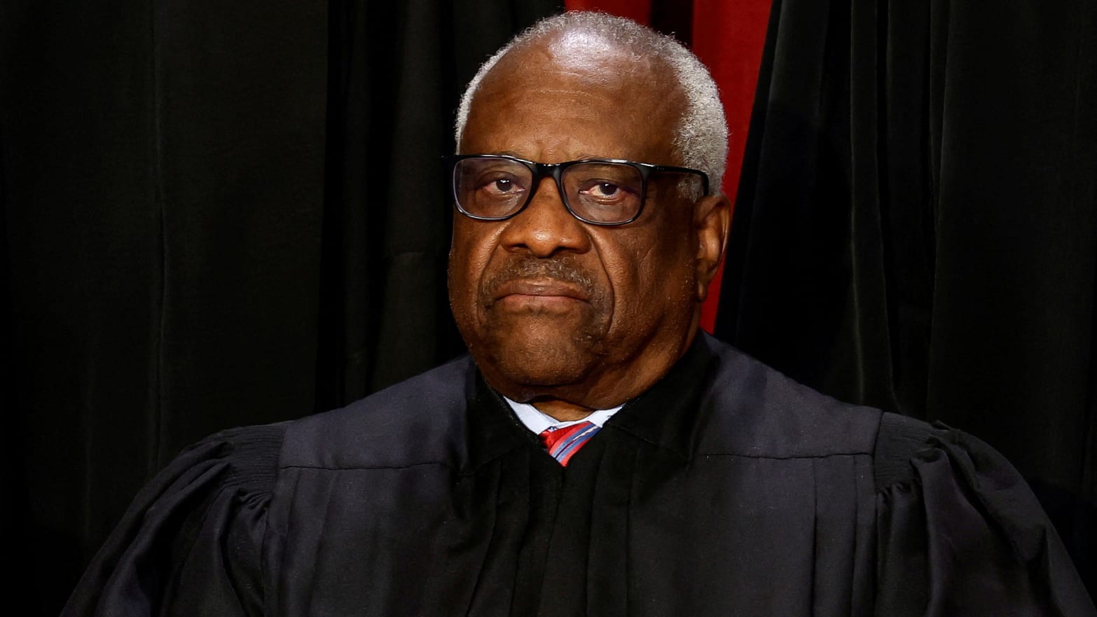 Clarence Thomas stares forward without smiling in a professional headshot.