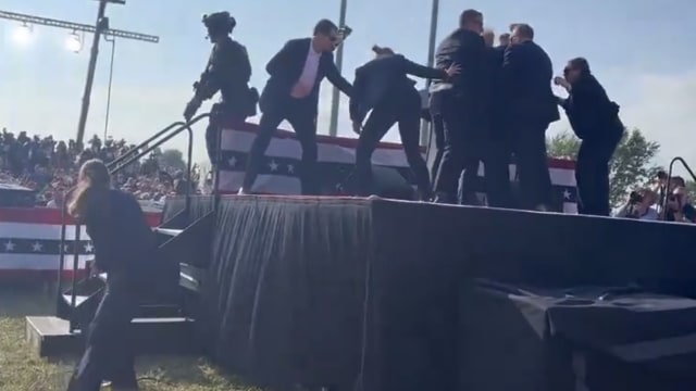 Behind-stage view of Secret Service agents shielding Donald Trump.