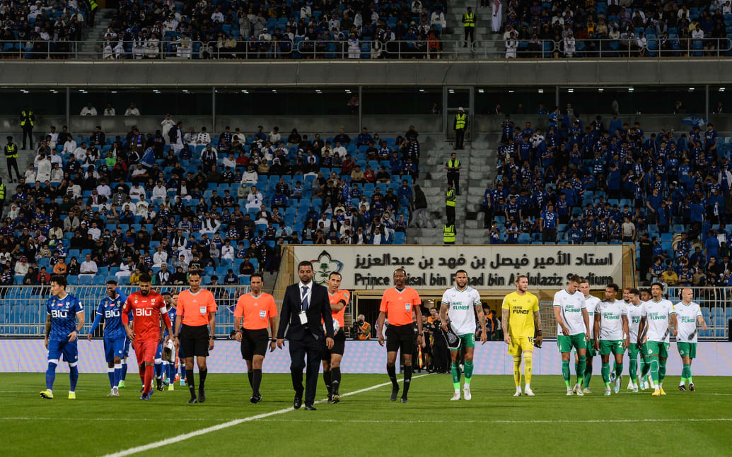A photo of Newcastle United FC and Al Hilal football players walking onto the field during a friendly match in Saudi Arabia in 2022.