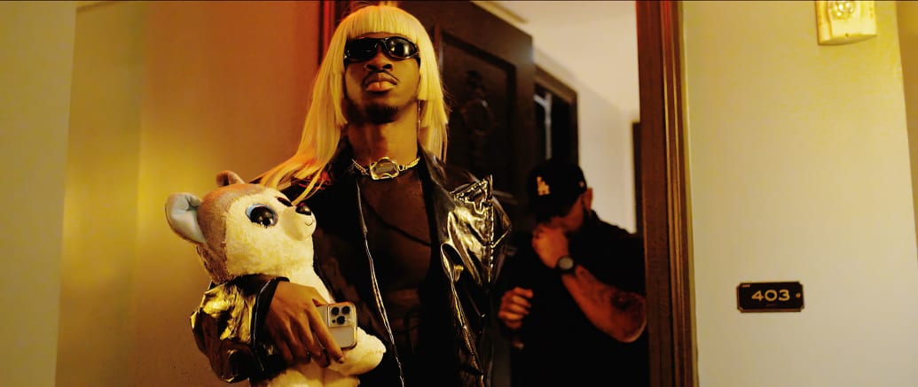 A picture of Lil Nas X wearing a blonde wig and holding a stuffed animal of a dog.