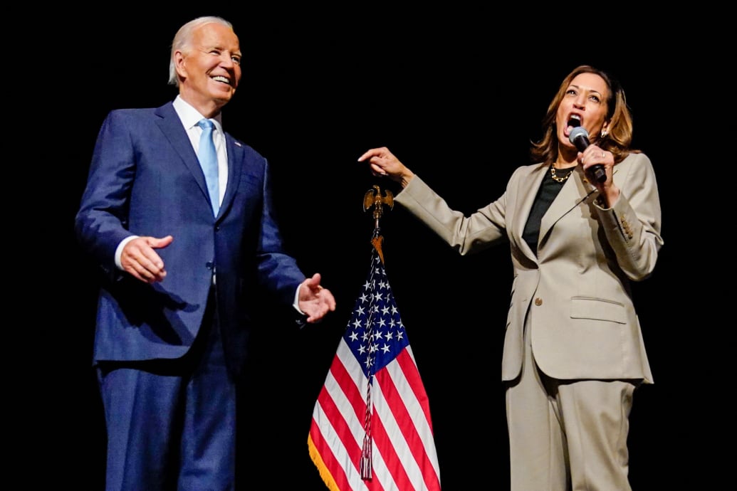 A photo of Joe Biden standing next to Kamala Harris as she speaks into a microphone.