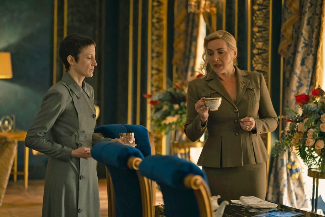 Kate Winslet drinks a cup of tea as she walks with Andrea Riseborough in a still from ‘The Regime’