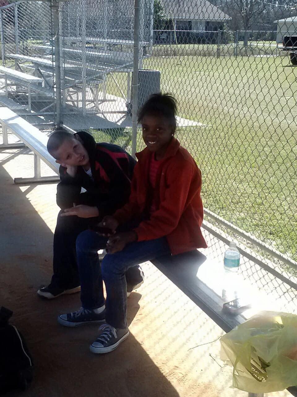 Logan Shubert, left, and Kennedy Sanders, right, sit on a bench in a softball dugout.