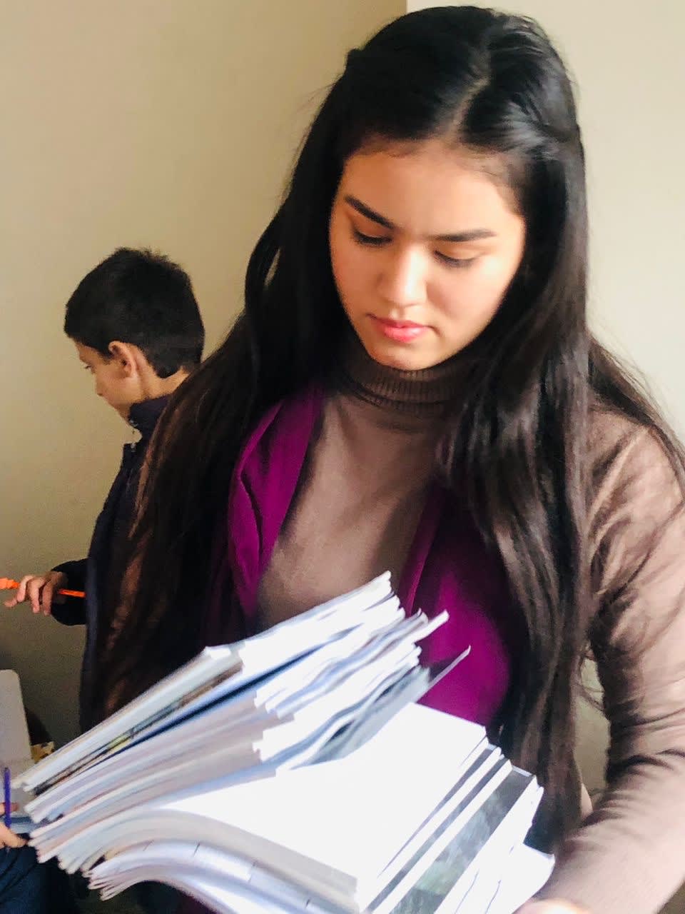 A girl stands holding a stack of papers