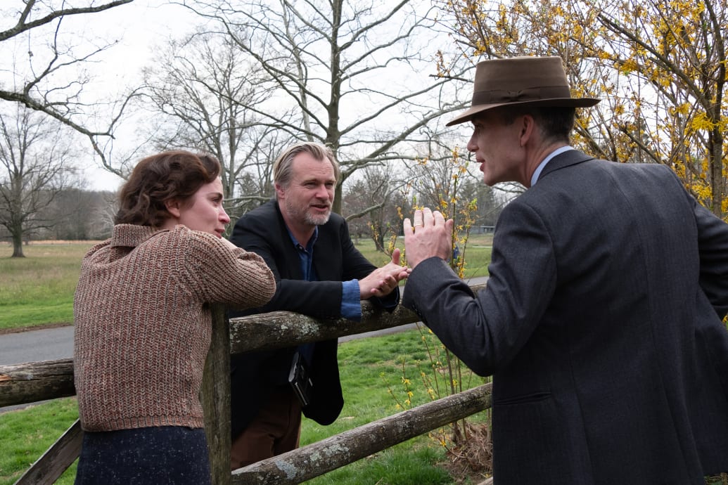 A behind-the-scenes image of Emily Blunt with writer, director, and producer Christopher Nolan and Cillian Murphy on the set of Oppenheimer.