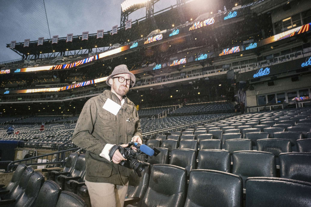 John Wilson filming at Mets Stadium in the rain. Embed 3: Mets fans.
