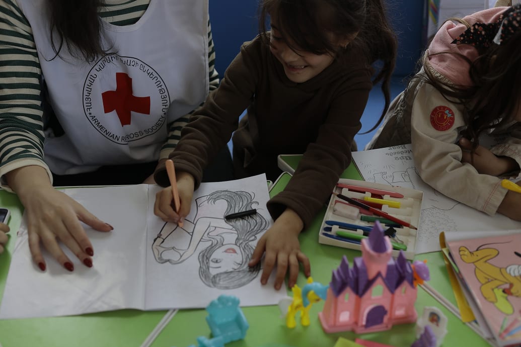 A Red Cross worker and children play with color books.