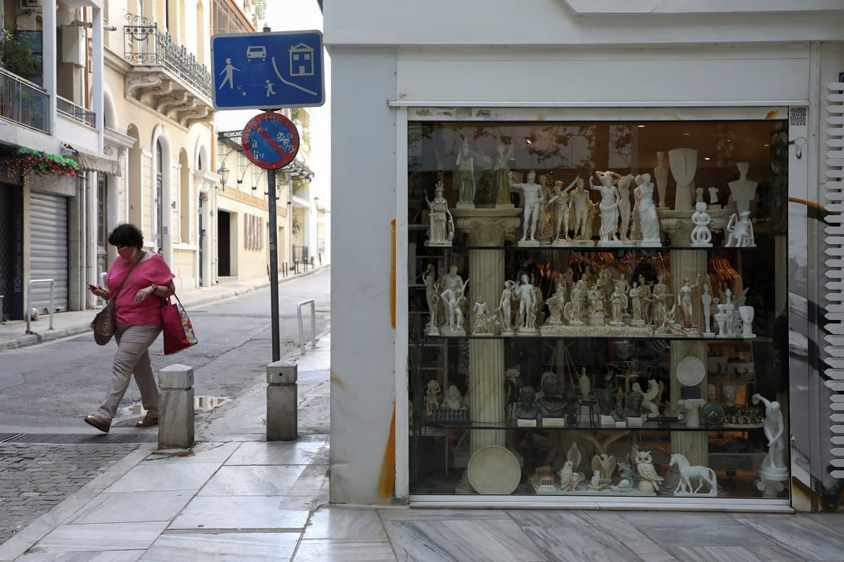 A woman wearing a protective face mask walks by a tourist shop in Plaka district