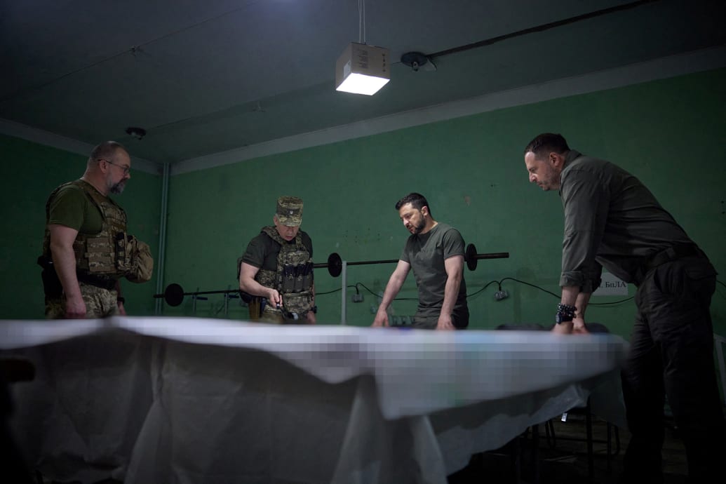 Ukraine President Volodymyr Zelensky looks over a map with military officers.