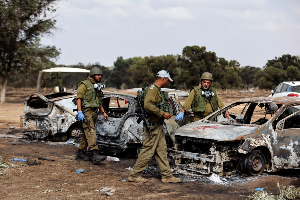 Israeli soldiers inspect the burnt cars of festival-goers at the site of an attack.