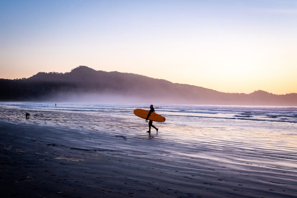 A surfer walks along the beach at Pacific Sands Beach Resort in Tofino, Canada.