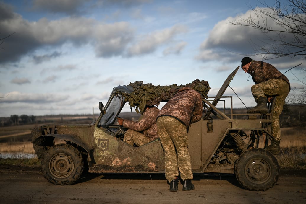 Kherson looks on as other soldiers try to repair a broken-down dune buggy.