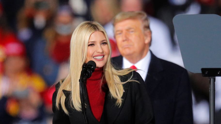 Ivanka Trump smiles at a podium in front of a blurred out Donald Trump and his supporters