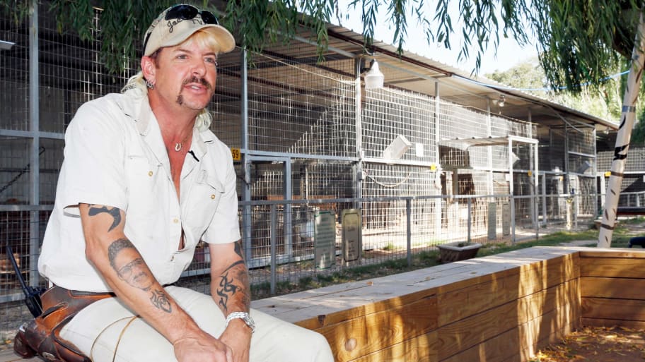 Joe Exotic sits near animal cages.