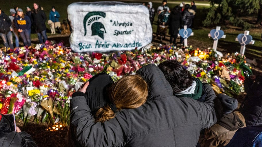 People comfort each other amongst bouquets of flowers during a vigil at The Rock on the Michigan State University campus 