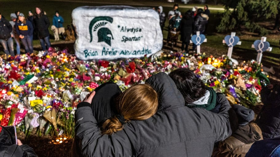 People comfort each other amongst bouquets of flowers during a vigil at The Rock on the Michigan State University campus.