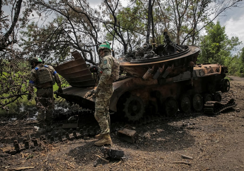 An image of Ukrainian soldiers look through the wreckage of a Russian armored vehicle in Ukraine.