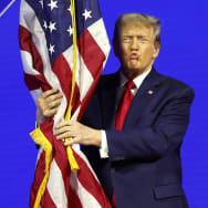 Republican presidential candidate and former U.S. President Donald Trump hugs an American flag as he arrives at the Conservative Political Action Conference (CPAC) at the Gaylord National Resort Hotel And Convention Center in National Harbor, Maryland