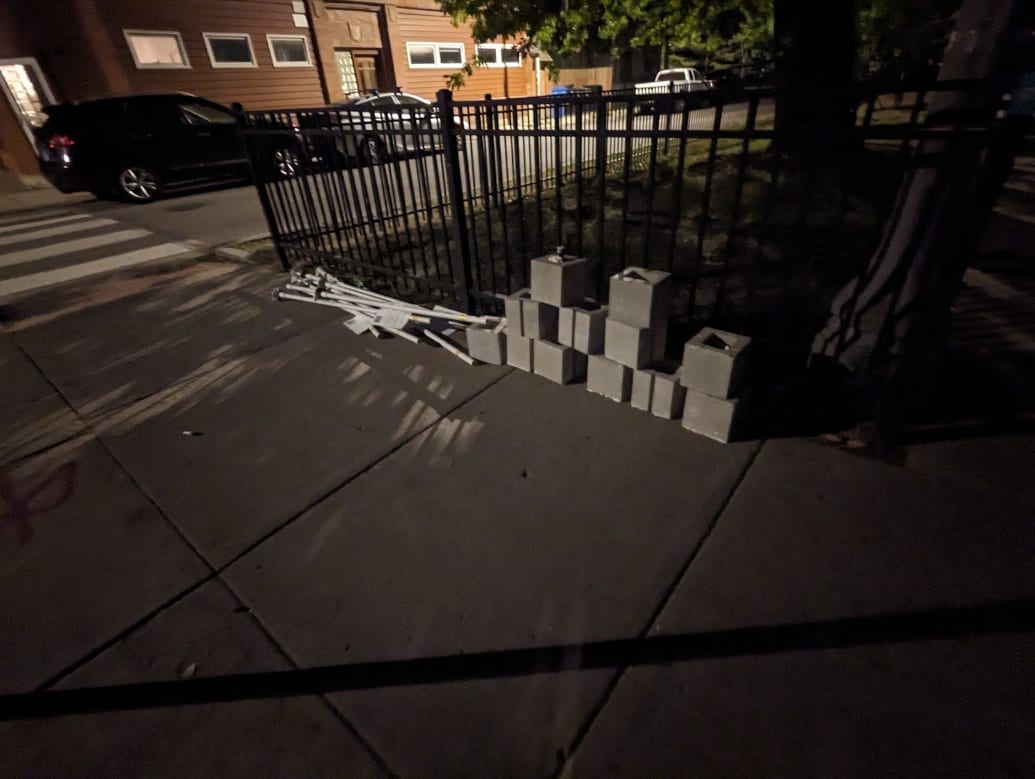 The equipment from the People's CDOT installation dismantled and placed on the sidewalk. A pile of cinder blocks in the foreground with PVC piping. 