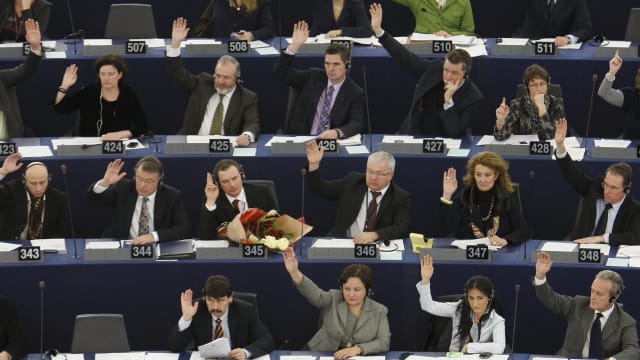 Members of the European Parliament vote with raised hands in seats.