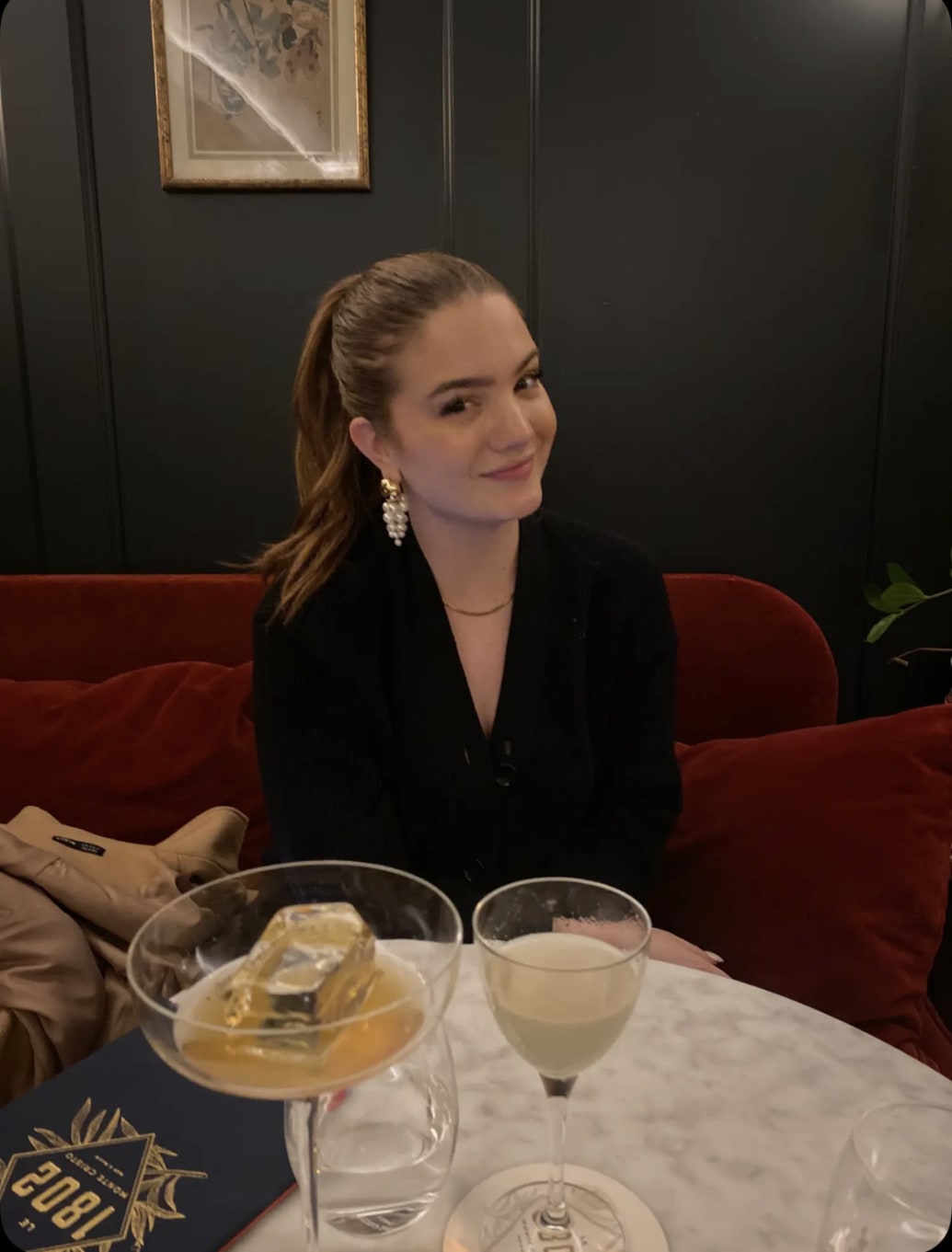 A young woman sits at a table with two cocktails in front of her. 