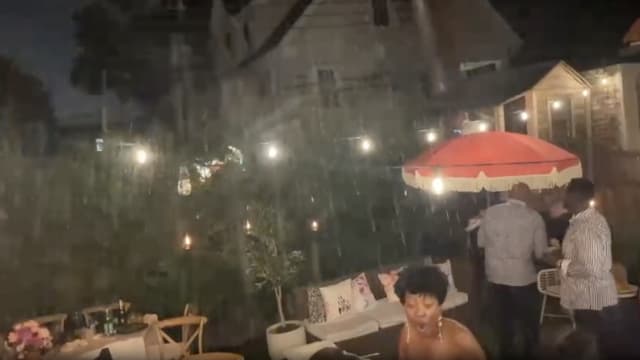 A screenshot from a video taken by a guest at a dinner party while a neighbor sprays their backyard with a hose.