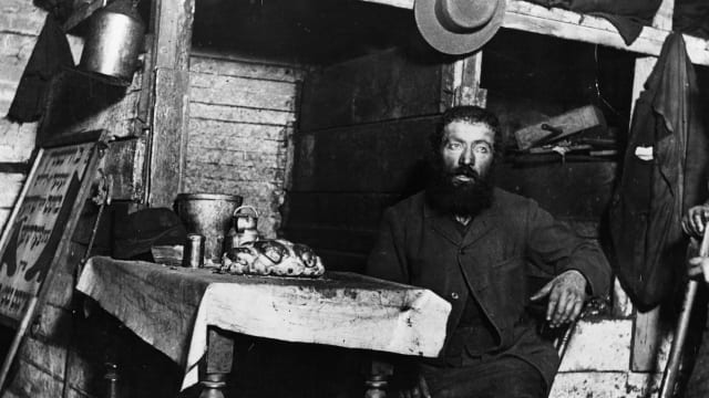 A photograph of a Jewish cobbler ready for Sabbath Eve in a coal cellar in New York, where he is living with his family taken by Jacob Riis.