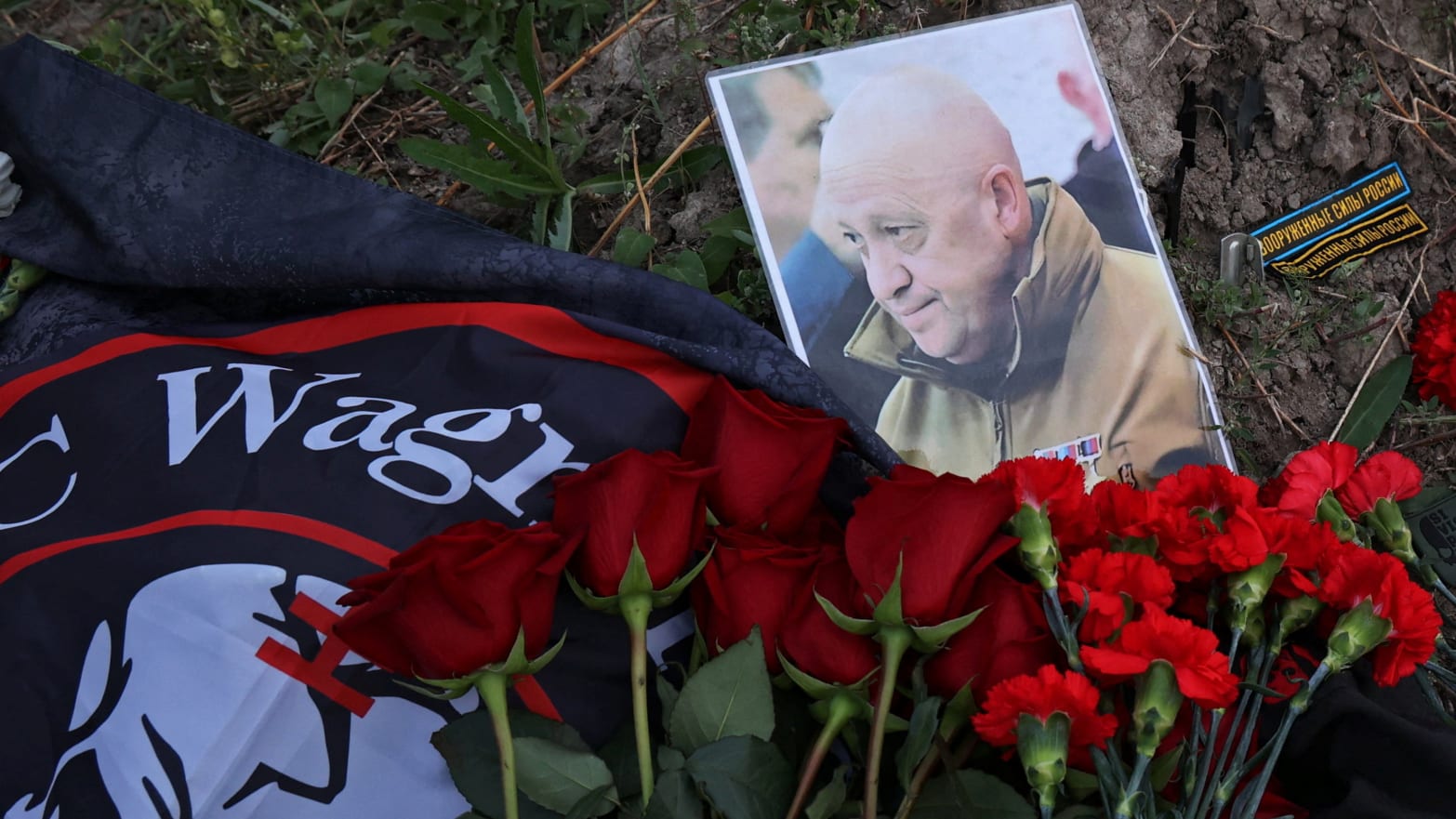 A photo of Yevgeny Prigozhin with the Wagner Group flag and red flowers.