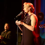 Kate Winslet stands at a microphone in a still from ‘The Regime’