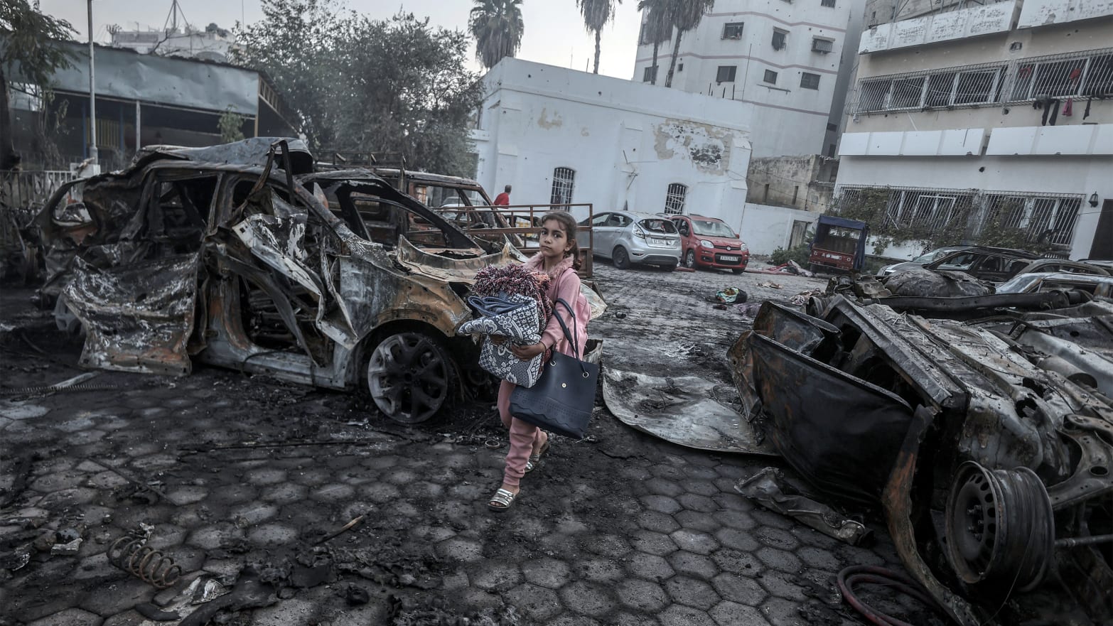 A girl tries to collect usable belongings amid wreckage of vehicles after Al-Ahli Baptist Hospital was hit in Gaza City, Gaza on Oct. 18, 2023.