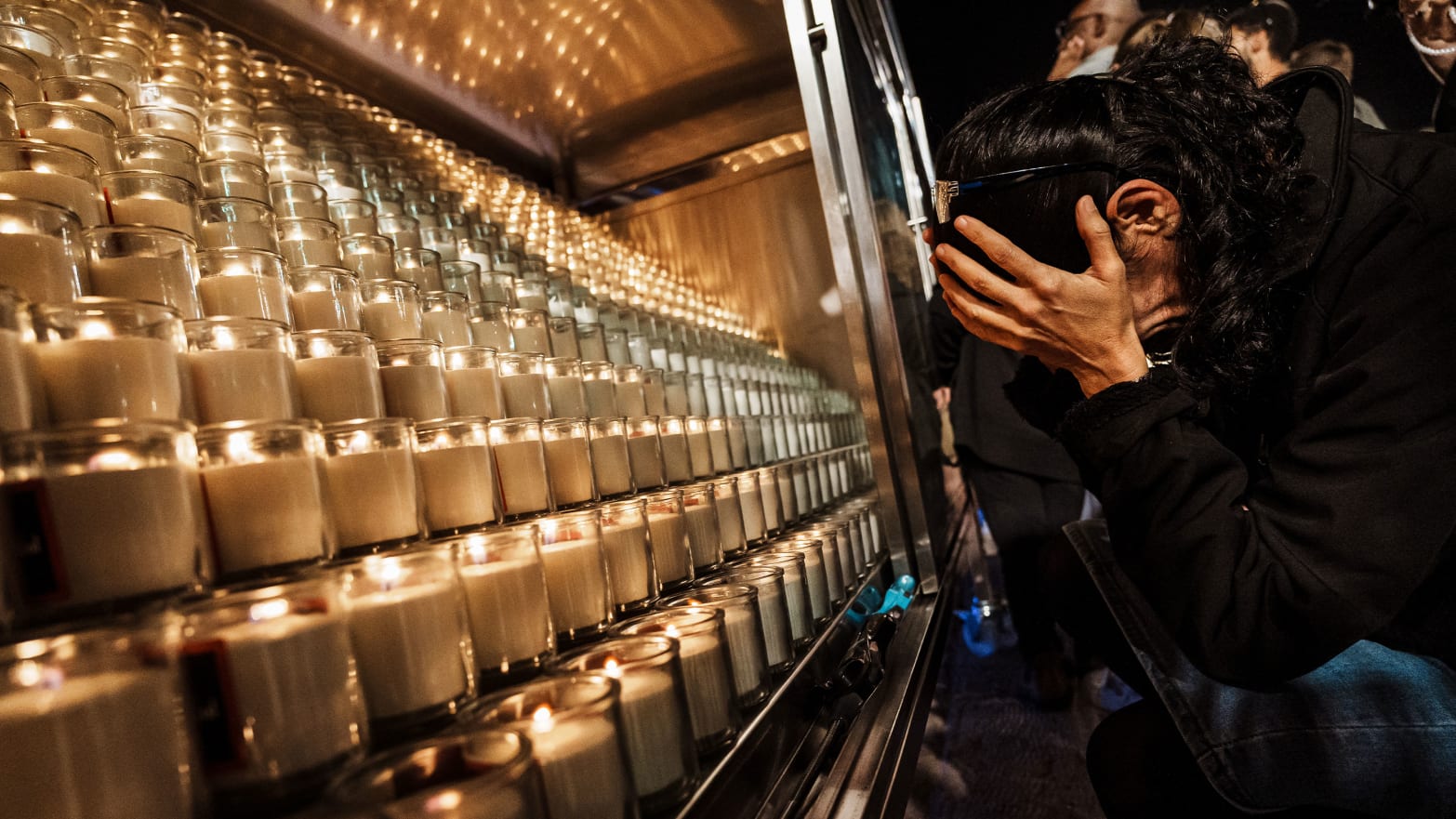 A picture of a woman weeps in her hands in front of rows of candles.