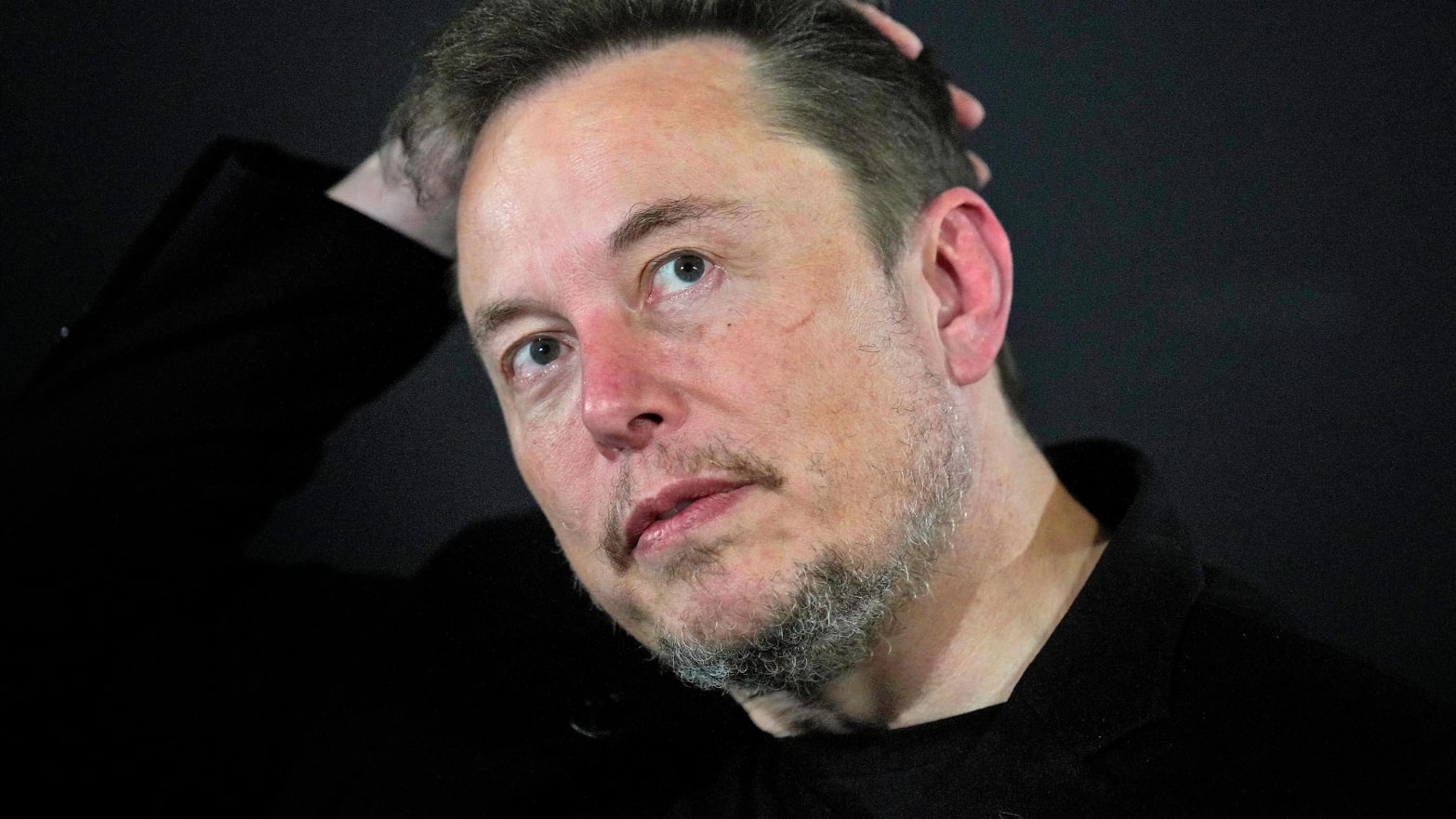 A close up of Elon Musk with his hand on his head