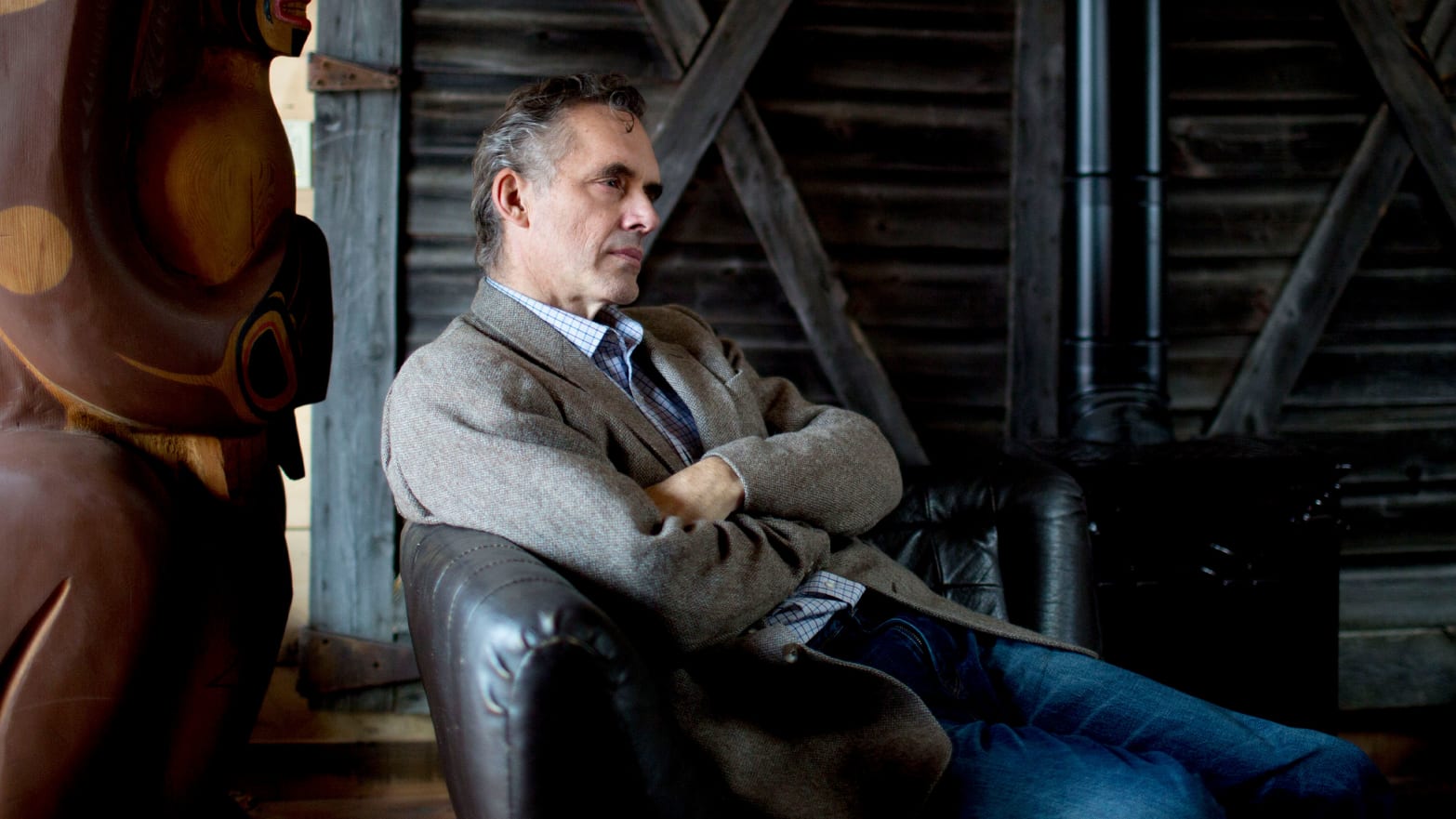 Jordan Peterson sits in a chair with his arms crossed