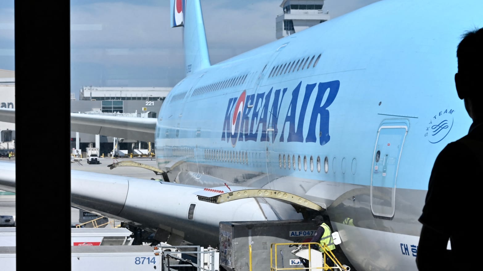 A photo of a Korean Air jetliner parked at the gate, as viewed from a window inside the terminal.