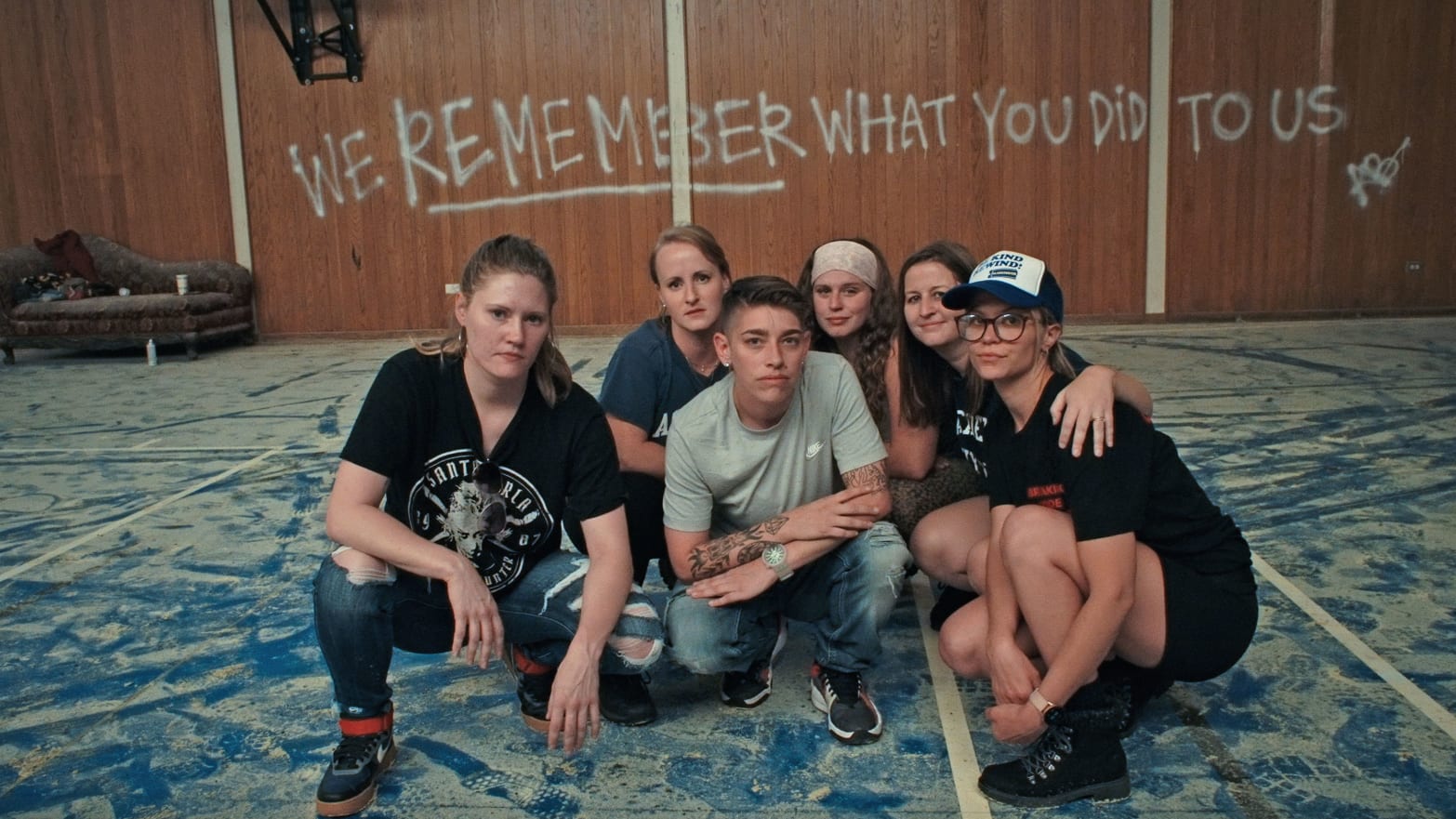 A group of women crowd together to pose for a picture in a room where the phase "we remember what you did to us" is spray painted on the walls