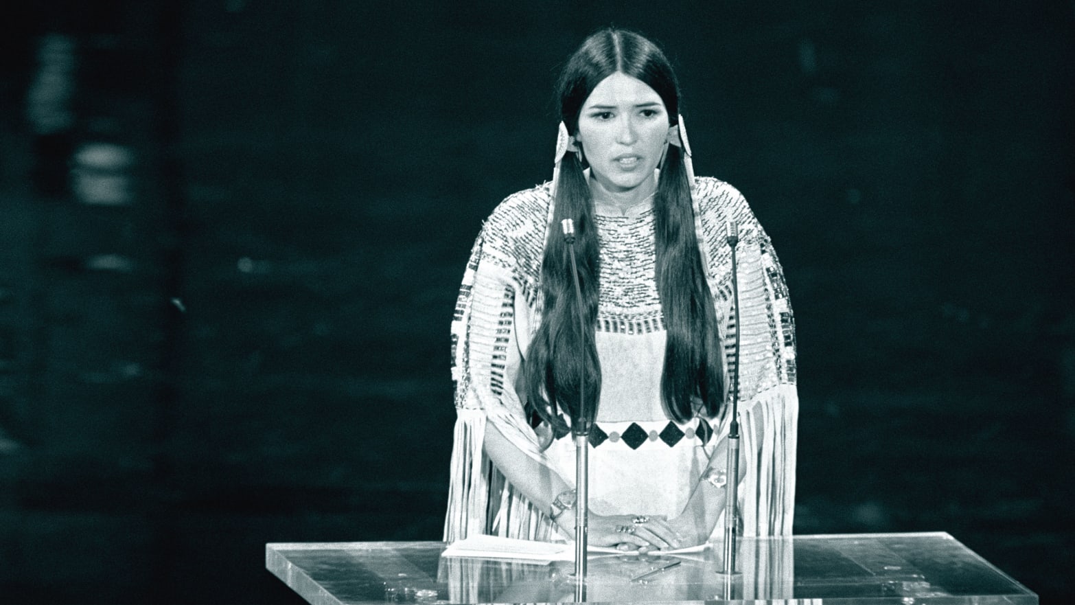An illustration including a photo of Sacheen Littlefeather speaking at the 45th Academy Awards.