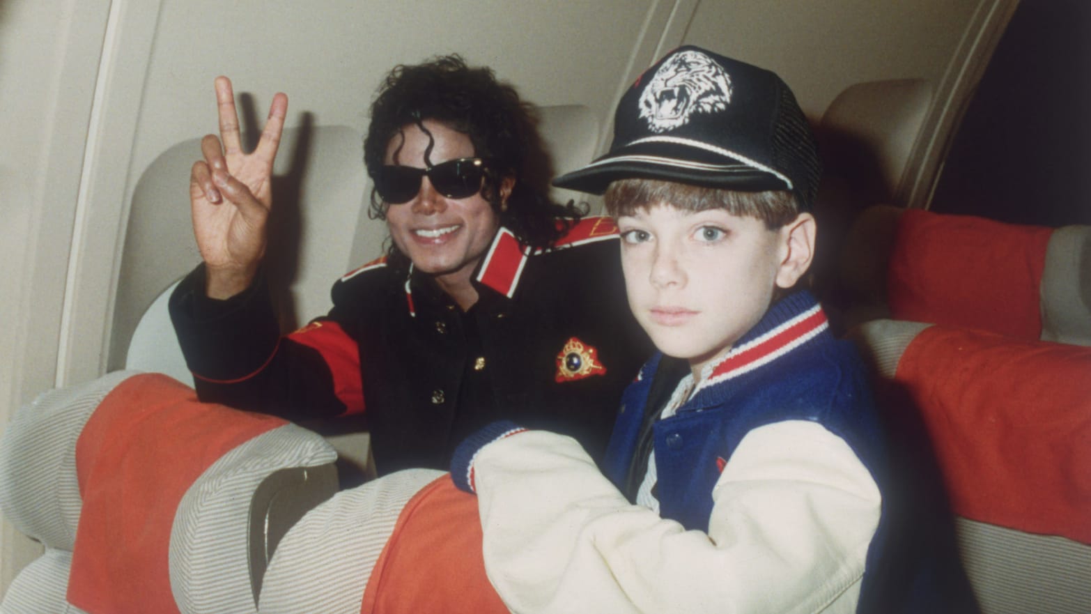 Michael Jackson throws a peace sign with Jimmy Safechuck on a tour plane